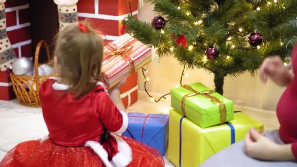 baby and pregnan mom hang red ball toy on Christmas tree. happy childhood concept. child and mother decorate tree with christmas balls. small child and a parent are playing by Christmas tree. - Footage, Video