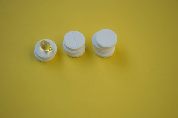 Close-up van goudkleurige olie supplementen, zachte gel capsule bovenop ronde witte pillen, gezondheidsconcept, farmaceutische tabletten - Foto, afbeelding