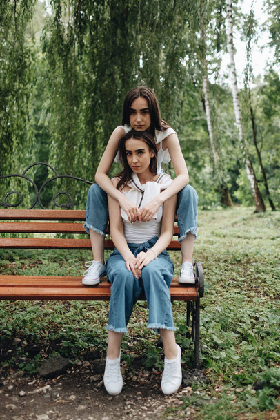 Portrait of Two Young Brunette Twins Sisters Dressed Alike in Jeans and White T-shirt, Best Friends Forever Concept - Photo, Image