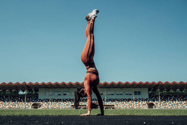 Porträt eines Sports Fitness Girls in modischer Sportbekleidung bei Handstandübung und Flips im Stadtstadion, gesundes Lifestylekonzept - Foto, Bild