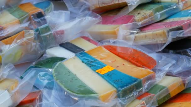 Intéressant fromage de vache dur multicolore et de chèvre de différents goûts à l'épicerie sur le marché. Fromage jaune, rouge, lavande, noir, vert
. - Séquence, vidéo