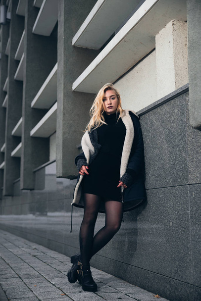 Girl in a black dress in the winter on a background of a dark building - Фото, изображение