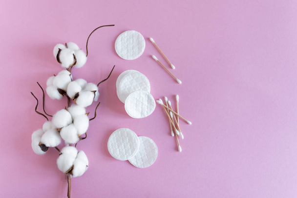 Baumwollstäbchen und Polster mit flauschigen Baumwollblumen auf rosa Hintergrund von oben. - Foto, Bild