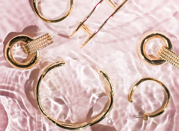 Golden bracelets, earrings, rings, jewelery on pink water backgr - Photo, Image