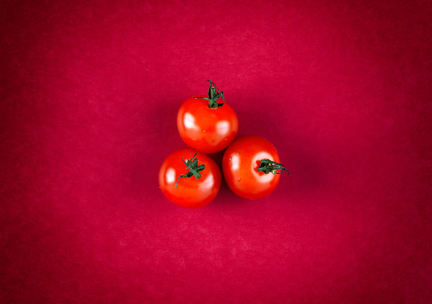 Three cherry tomatoes on red background. - Foto, Imagen