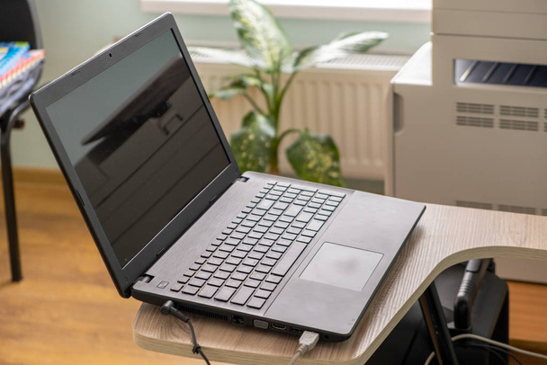 Computador portátil preto aberto em uma tabela pequena da cadeira no escritório inte
 - Foto, Imagem