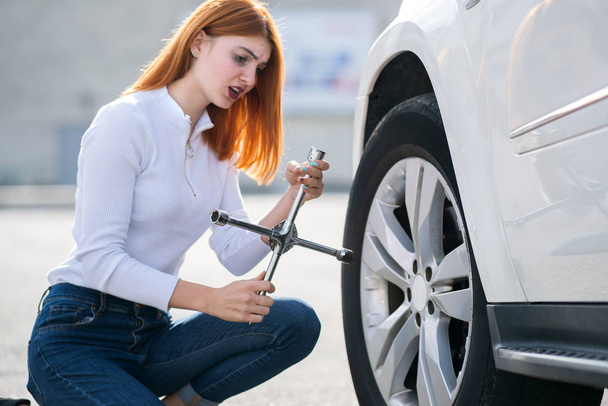Young woman with wrench changing wheel on a broken car. - Фото, изображение