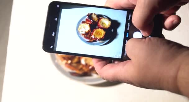 Νεαρός φωτογραφίζει μεσημεριανό στο εστιατόριο με το τηλέφωνο. Ένας νεαρός άνδρας φωτογραφίζει κέικ σε smartphone, φωτογραφίζοντας γεύμα με κινητή κάμερα. - Πλάνα, βίντεο