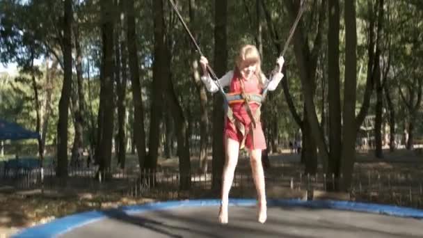 Κορίτσι παιδί άλμα στερεώνεται σε ένα τραμπολίνο στο πάρκο το καλοκαίρι. - Πλάνα, βίντεο