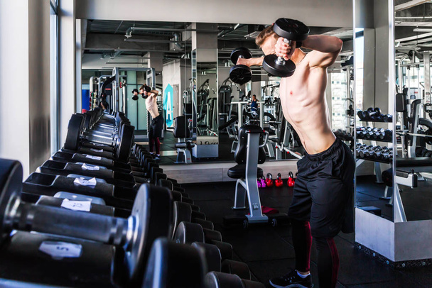 Athletic man with a naked torso in the gym lifts dumbbells.  - Valokuva, kuva
