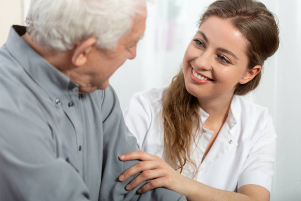 Smiling young nurse sitting at table with senior patient - Photo, Image