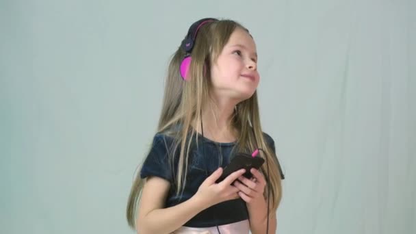 Pretty smiling cild girl listening to music in big pink earphones. - Filmati, video