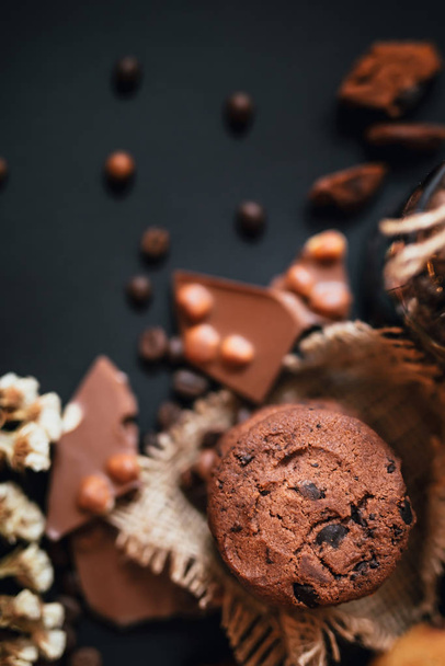 Galletas de pan corto con trozos de chocolate, chocolate con leche con nueces y granos de café sobre un fondo negro
. - Foto, imagen