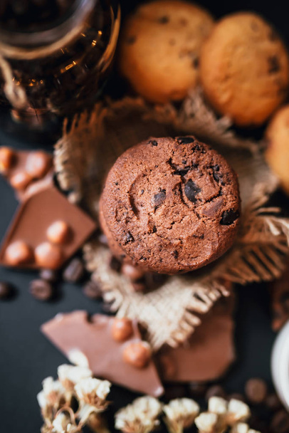 Shortbread koekjes met chocoladestukjes, melkchocolade met noten en koffiebonen op een zwarte achtergrond. - Foto, afbeelding