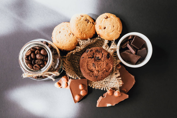 Μπισκότα με κομματάκια σοκολάτας, σοκολάτα γάλακτος με ξηρούς καρπούς και κόκκους καφέ σε μαύρο φόντο. - Φωτογραφία, εικόνα