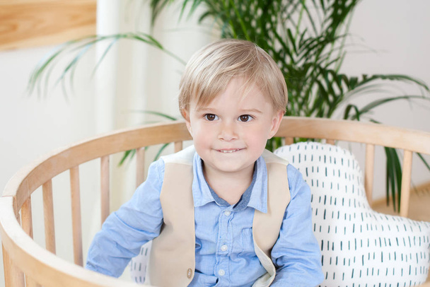 little boy. Portrait of a happy boy playing in a baby cot. The boy sits alone in a crib in the nursery. The lonely child stays in the crib. Loneliness. The baby in bed is smiling. Portrait of a child. - Fotoğraf, Görsel