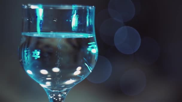 Christmas, New year, Holidays. Bubbles in a champagne glass against a background of flickering colored lights. Background video. Slow motion. Close up. Macro. - Footage, Video