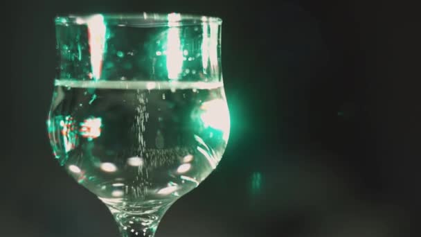 Kerstmis, Nieuwjaar, feestdagen. Bubbels in een champagneglas tegen een achtergrond van flikkerende gekleurde lichten. Achtergrond video. Langzame beweging. Sluit maar af. Blauwe wijting. - Video