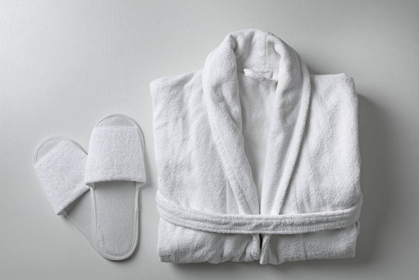 Clean folded bathrobe and slippers on white background, flat lay - Фото, изображение