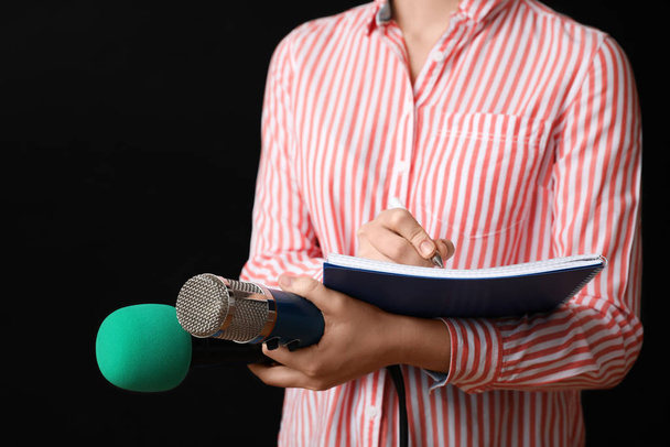 Journalist with microphones and notebook on black background, closeup - Φωτογραφία, εικόνα