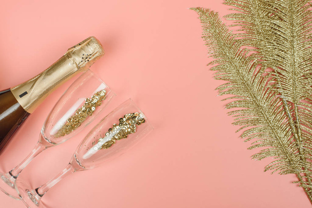 Butelka szampana, szklanki i złote palmy stylowe gałęzie ze złotym konfetti na różowym pastelowym tle. Widok góry. Boże Narodzenie, urodziny lub koncepcja ślubu - Zdjęcie, obraz