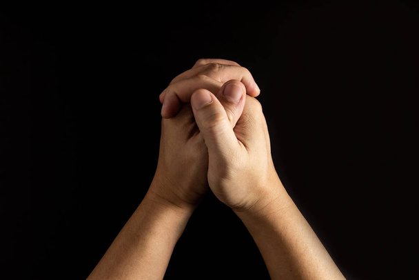A férfi keze, aki fogja a kezét, imádkozik, fekete hátvédje van. - Fotó, kép