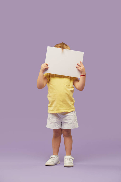 Little child boy holding a white banner on purple background. Funny Face. Copy space for text - Foto, Bild