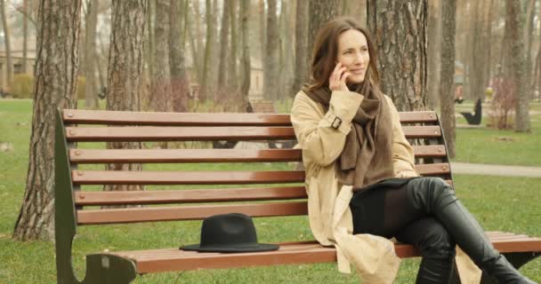 秋の公園のベンチに座って電話で話す美しい女の子が笑顔で会話を楽しむ. - 映像、動画