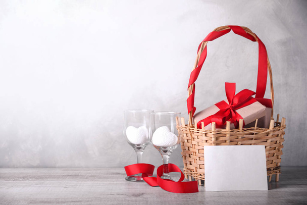 Tarjeta de felicitación San Valentín con corazones, copa y regalos en cesta sobre fondo de madera. Con espacio para tus saludos de texto
 - Foto, imagen