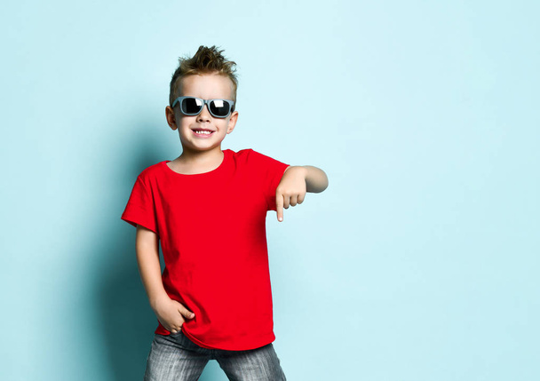 Serious boy in bright stylish casual clothing and sunglasses standing over blue background - Zdjęcie, obraz