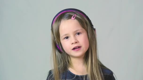 Bastante chica cild sonriente escuchando música en grandes auriculares rosados
. - Imágenes, Vídeo