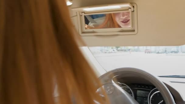 Młoda ruda kierowca kobieta za kierownicą sprawdza jej makijaż w lusterku wstecznym. - Materiał filmowy, wideo