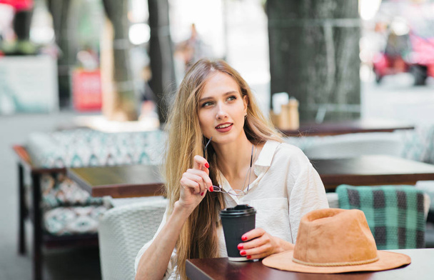 Веселая улыбчивая женщина сидит в уличном кафе и пьет кофе - Фото, изображение