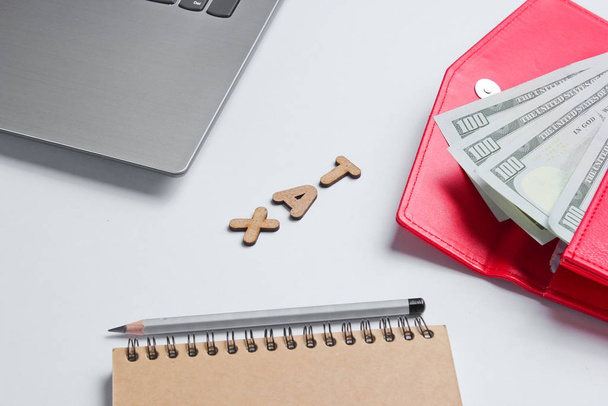 Kreatives Geschäftskonzept. Laptop, Notizbuch, Bleistift, Brieftasche mit Dollarscheinen auf weißem Hintergrund mit dem Wort Steuer aus Holzbuchstaben, Minimalismus - Foto, Bild