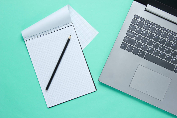 Minimalistyczna koncepcja biznesu. Laptop, notatnik z ołówkiem na niebieskim tle. Widok z góry - Zdjęcie, obraz