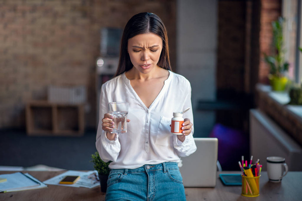 Cheerless young woman holding pills in her hand - Foto, afbeelding