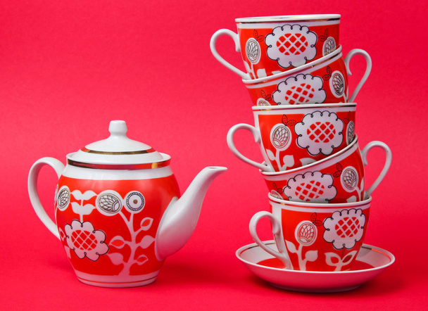 Stapel von Retro-Keramik-Tassen und Teekanne auf rotem Hintergrund. Ansicht von oben - Foto, Bild