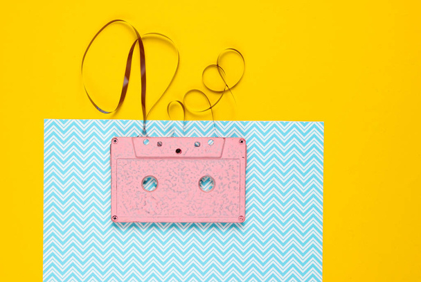 Music lover minimalism concept. Retro style 80s. Pink audio cassette with film on a blue yellow paper background. - Valokuva, kuva