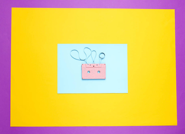 Musikliebhaber Minimalismus Konzept. 80er Jahre im Retro-Stil. Pinkfarbene Audiokassette mit Film auf farbigem Papierhintergrund. Ansicht von oben - Foto, Bild