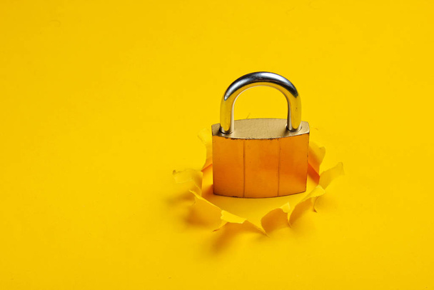 Metal lock through a torn hole on yellow paper background - Foto, immagini