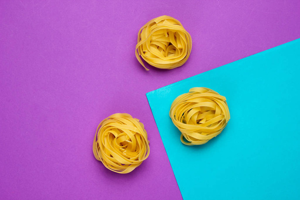 Minimalismo concepto de comida italiana. Fideos tagliatelle crudos sobre fondo azul-púrpura
 - Foto, imagen