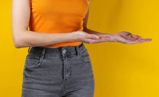 Woman shows her palm for copy space on yellow background. Crop photo, studio shot - Foto, afbeelding