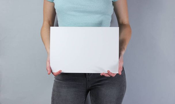Woman holding white empty sheet of paper for copy space on gray  background. Crop photo, studio shot - Фото, изображение