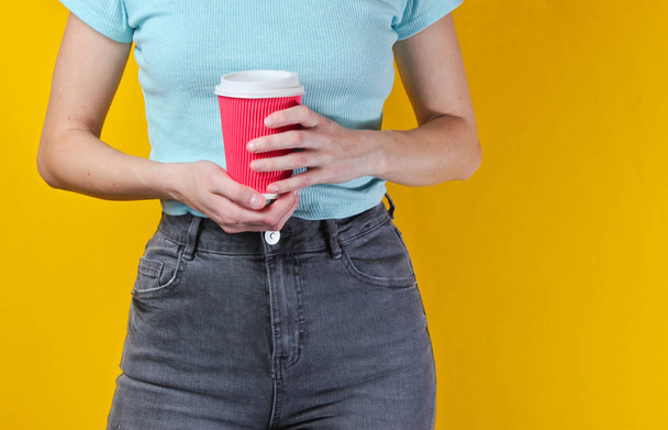 Woman holding cardboard  cup of coffee on yellow background. Crop photo, studio shot - Foto, Imagem