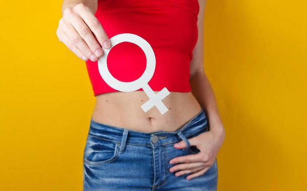 Femen concept. Vrouw houdt in haar hand genderfeminisme symbool op gele achtergrond. Foto bijsnijden, studio opname - Foto, afbeelding