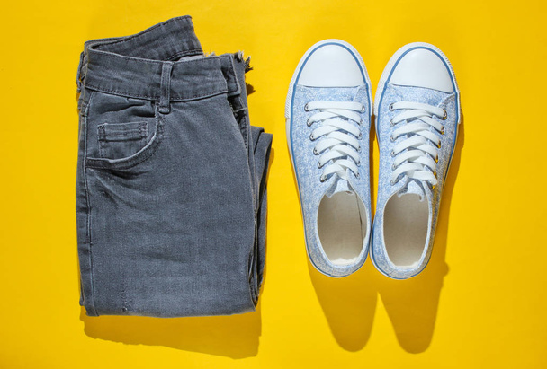 Minimalism fashion concept. Fashionable sneakers and jeans on a yellow background. Top view - Photo, Image
