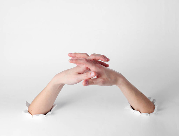 Woman stretches her fingers through the torn holes of a white background. Creative art - Foto, Imagen