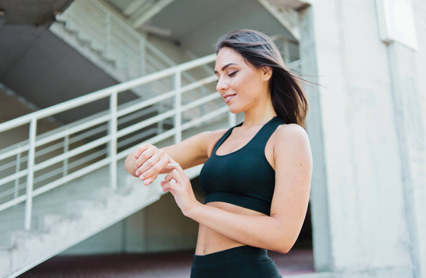 Приваблива спортивна жінка в спортивному одязі використовує розумний годинник на відкритому повітрі в міському середовищі
 - Фото, зображення
