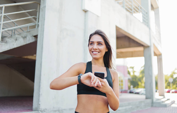 Atractiva mujer deportiva en ropa deportiva usar reloj inteligente al aire libre en el entorno urbano
 - Foto, imagen