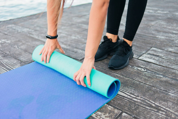 Closeup of female hands reeling in yoga mat on the beach. Healthy lifestyle concept - Photo, Image